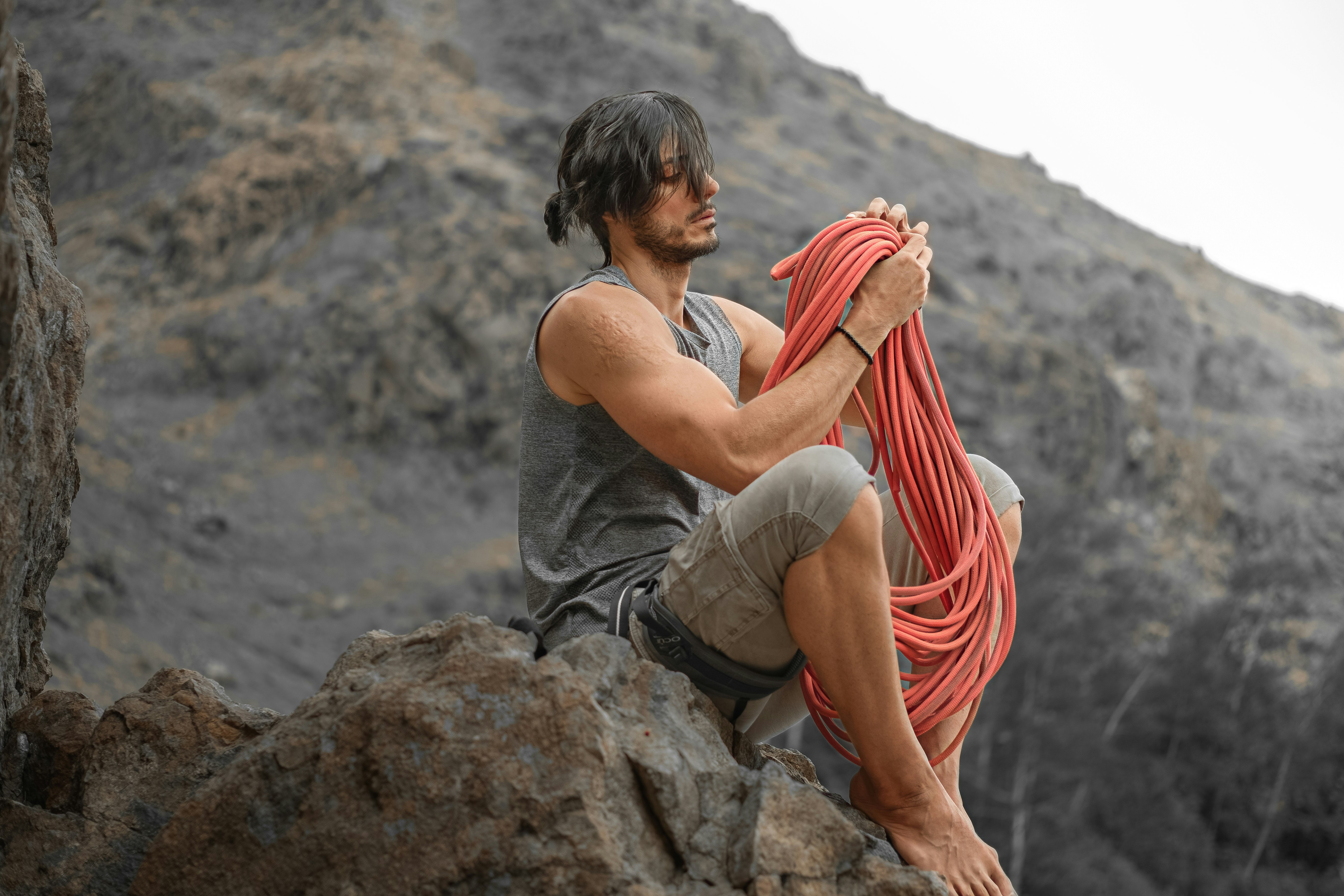 man in gray tank top sitting on rock during daytime